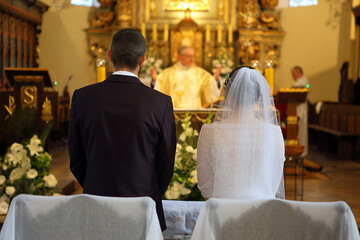 A young couple stands in front of the altar during a wedding ceremony in a Catholic church. - 624403518