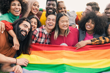 Young diverse friends having fun holding LGBT rainbow flag - Multiracial people hugging each other...
