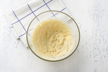 Glass bowl with whipped butter and sugar on a light blue background, top view. Cooking homemade milk cakes, do it yourself, step by step, step 2