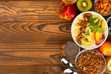 Granola bowl with yogurt and fresh almonds, blueberries, raspberries,peach, kiwi, strawberries and banana on textured kitchen table.Acai and spirulina bowl.Healthy breakfast concept. Copy space.