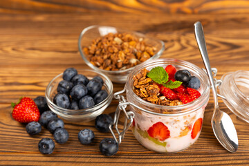 Granola bowl with yogurt and fresh almonds, blueberries, raspberries,peach and strawberries on a brown kitchen table.Acai and spirulina bowl.Healthy breakfast concept.