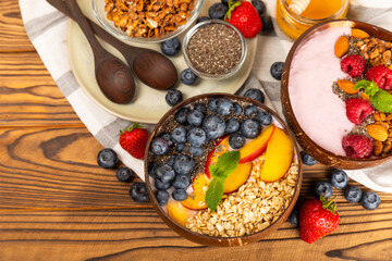 Granola bowl with yogurt and fresh almonds, blueberries, raspberries,peach and strawberries on a brown kitchen table.Acai and spirulina bowl.Healthy breakfast concept.