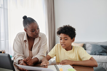 African American mother helping her son to do homework while they sitting at table in the room
