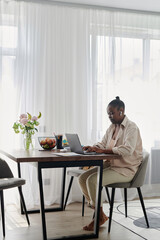 Vertical image of African American woman working online on laptop at home