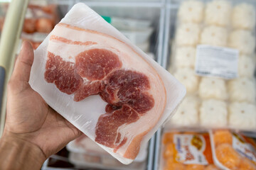 Close-up of man's hand holding frozen pork meat in supermarket.