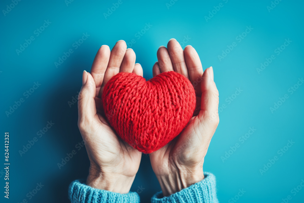 Wall mural elderly female hands holding a knitted red heart made of threads.ai generative