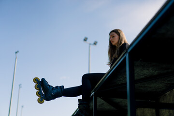 sporty girl after rollerblading rests on the sports ground thoughtful and happy with the street...