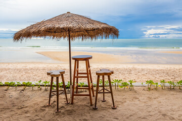 Set of wooden tables and chairs and leaf umbrellas for sitting and drinking drinks by the beach with sky and tide waves.