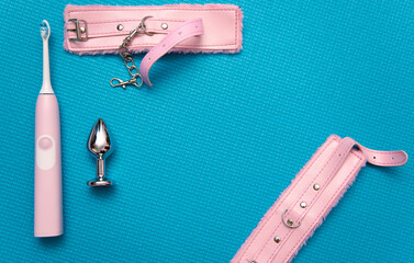 Sex toys on a blue background. Anal plug with pink handcuffs and electric toothbrush. Household appliances for sex. Sex concept.