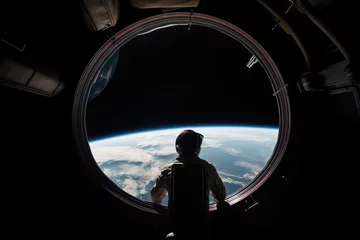 Fotobehang Astronaut stand near round window with view on earth in space station in space © Oleksandr Kozak