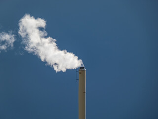 View of a huge metal chimney with white and grey dense smoke from burning firewood, pellets or briquettes