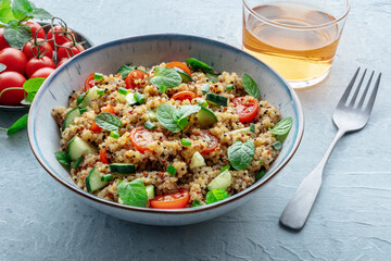 Fototapeta na wymiar Quinoa tabbouleh salad in a bowl, a healthy dinner with tomatoes and mint, with a drink
