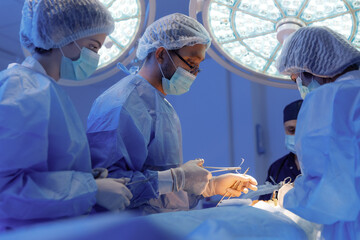 Three medical surgeons in scrubs and one standing at the head of the patient in dark blue scrubs...