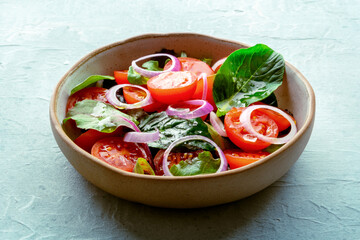 Salad with tomato, fresh leaves, and onions, on a slate background. Healthy diet, simple vegan recipe