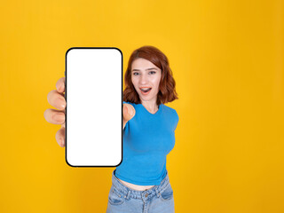 Showing modern smartphone, lovely excited positive caucasian woman with red hair showing modern smartphone. Empty blank white screen mobile phone mock up. Isolated yellow background, copy space.
