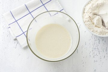 A glass bowl with a whipped mass of eggs, butter, sugar and milk on a light blue background, top view. Cooking homemade milk cakes, do it yourself, step by step, step 5