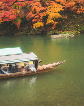 Katsura River, Kyoto, Japan - 23 November 2022: View of people on a boat tour crossing the Katsura River from Kameyama Park in Kyoto, Japan.