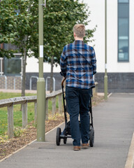 Young English father in plaid shirt walks with pram on summer day. Authentic, back view, urban parenting, family, happiness. Vertical crop.