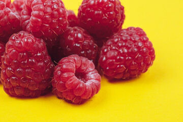 Heap of fresh ripe and sweet raspberries on yellow background. Red raspberries. Macro shot.