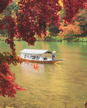 Katsura River, Kyoto, Japan - 23 November 2022: View of people on a boat tour crossing the Katsura River from Kameyama Park in Kyoto, Japan.