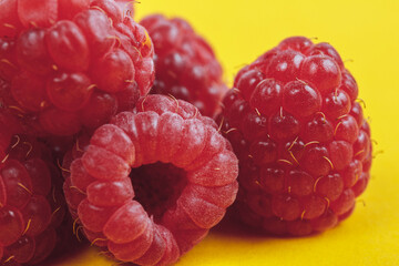 Heap of fresh ripe and sweet raspberries on yellow background. Red raspberries. Macro shot.