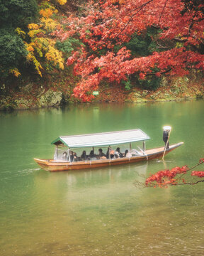 Katsura River, Kyoto, Japan - 23 November 2022: View of people on a boat tour crossing the Katsura River from Kameyama Park in Kyoto, Japan.