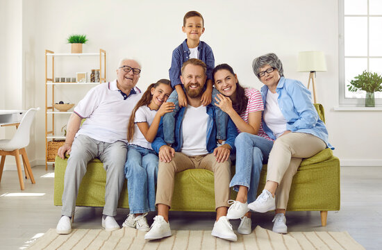Portrait of happy, friendly and loving family of three generations sitting together on sofa at home. Elderly parents and their adult children and grandchildren smile for camera while posing in room.