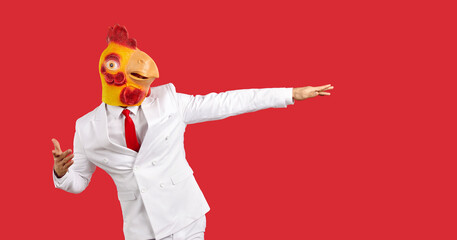 Funny humorus man in rubber mask rooster having fun dancing isolated on red background. Young man...
