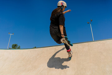young skilled woman rollerblading and jumping on the ramp in the skate park outside Practicing her...