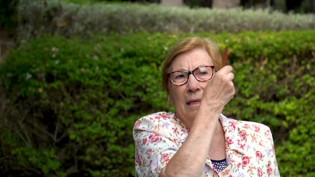 An older woman preens her hair with a comb, outdoors.