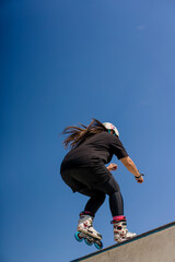 young skilled woman rollerblading and jumping on the ramp in the skate park outside Practicing her tricks or technique of rollerblading for competition