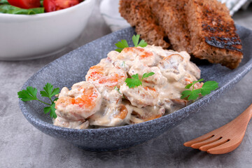 Shrimps in creamy sauce with champignons served on a plate with toasted bread and salad. Seafood meal