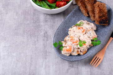 Shrimps in creamy sauce with champignons served on a plate with toasted bread and salad. Seafood meal