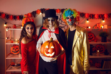 Portrait of cheerful adult friends with glowing jack-o-lantern in hands at Halloween party. Men...