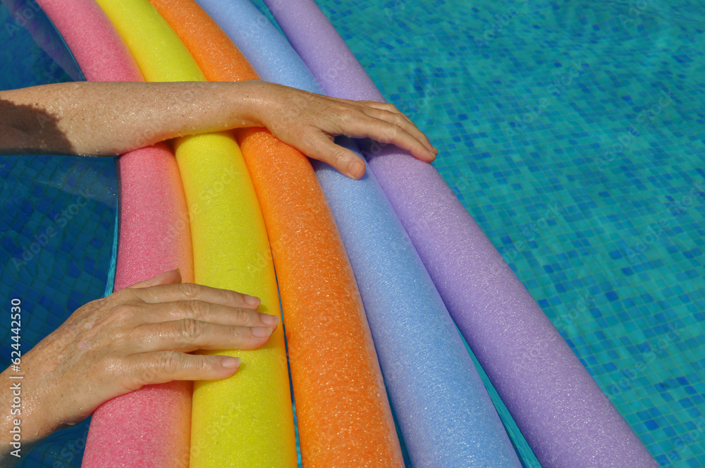 Wall mural Hands on rainbow pool noodles in swimming pool