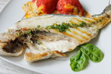 Grilled gilt-head bream on a white plate accompanied by stuffed piquillo peppers