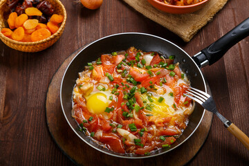 fresh shakshuka in a frying pan sprinkled with green onions on a laid Shabbat table.