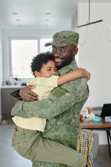 Vertical image of little son embracing his dad in military uniform, he meeting him from war at home