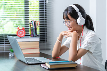 Happy smiling female student wearing headphones talking in online discussion meeting using laptop in home office. female college student studying distance education business