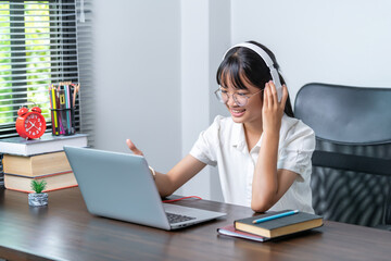 Happy smiling female student wearing headphones talking in online discussion meeting using laptop in home office. female college student studying distance education business