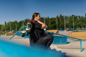 young hipster girl sitting in skate park with roller skates before starting training lesson on...