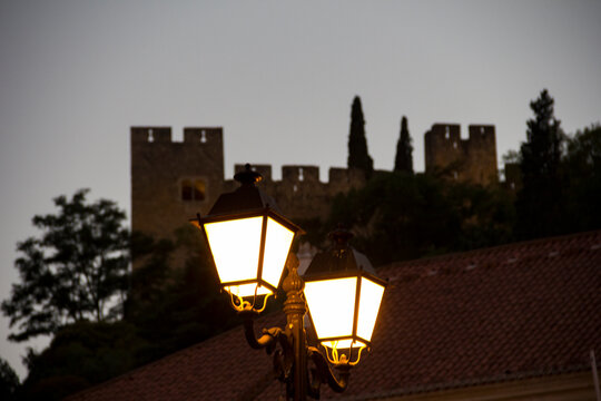 Candelabros de rua acesos &agrave; frente de muralhas e &aacute;rvores 