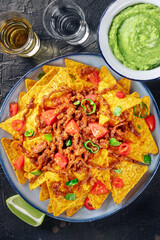 Nachos, Mexican food, tortilla chips with beef and fresh vegetables, overhead flat lay shot with tequila and guacamole sauce