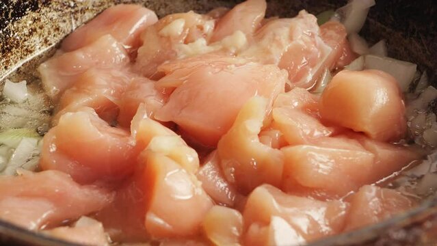 Chicken pieces fried in a cast-iron skillet in oil with onions. Close-up