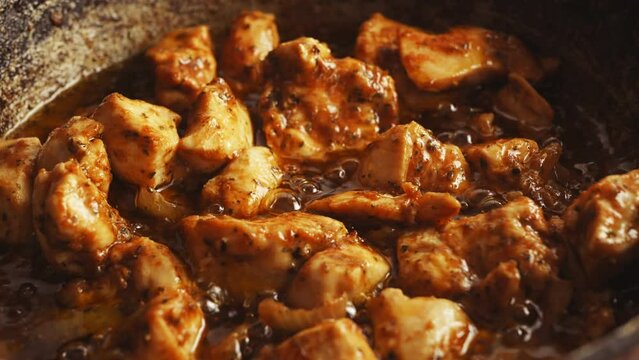 Chunks of chicken in spices fried in a cast-iron skillet in oil gurgle. Close-up