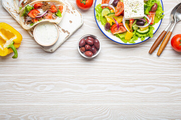Traditional Greek Food: Greek Salad, Gyros with meat and vegetables, Tzatziki sauce, Olives on White rustic wooden table background from above. Cuisine of Greece. Copy space