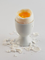 Broken and peeled white egg with runny yolk in a white egg cup
