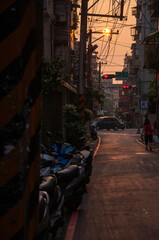Pedestrians and motor vehicles crowded in the narrow alleyway under the sunset