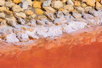 Salt-encrusted stones and pink water in the salt flats near Aigues-Mortes in the Camargue region