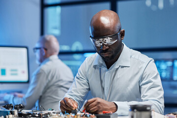 African American engineer in protective glasses working with computer board at table in the lab